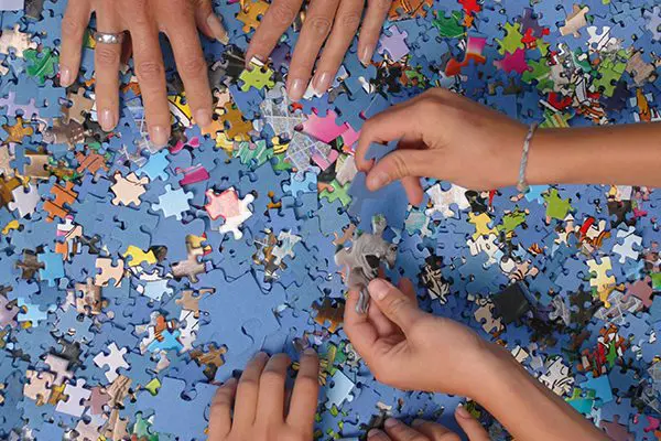 Ein Foto zeigt mehrere Hände, die gemeinsam ein Puzzle zusammensetzen.