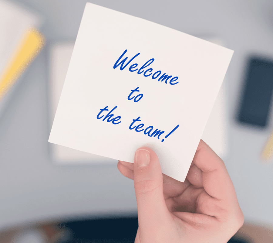 Eine Grafik zeigt eine Hand, die einen kleinen weißen Zettel hält. Auf dem Zettel steht "Welcome to the team!"