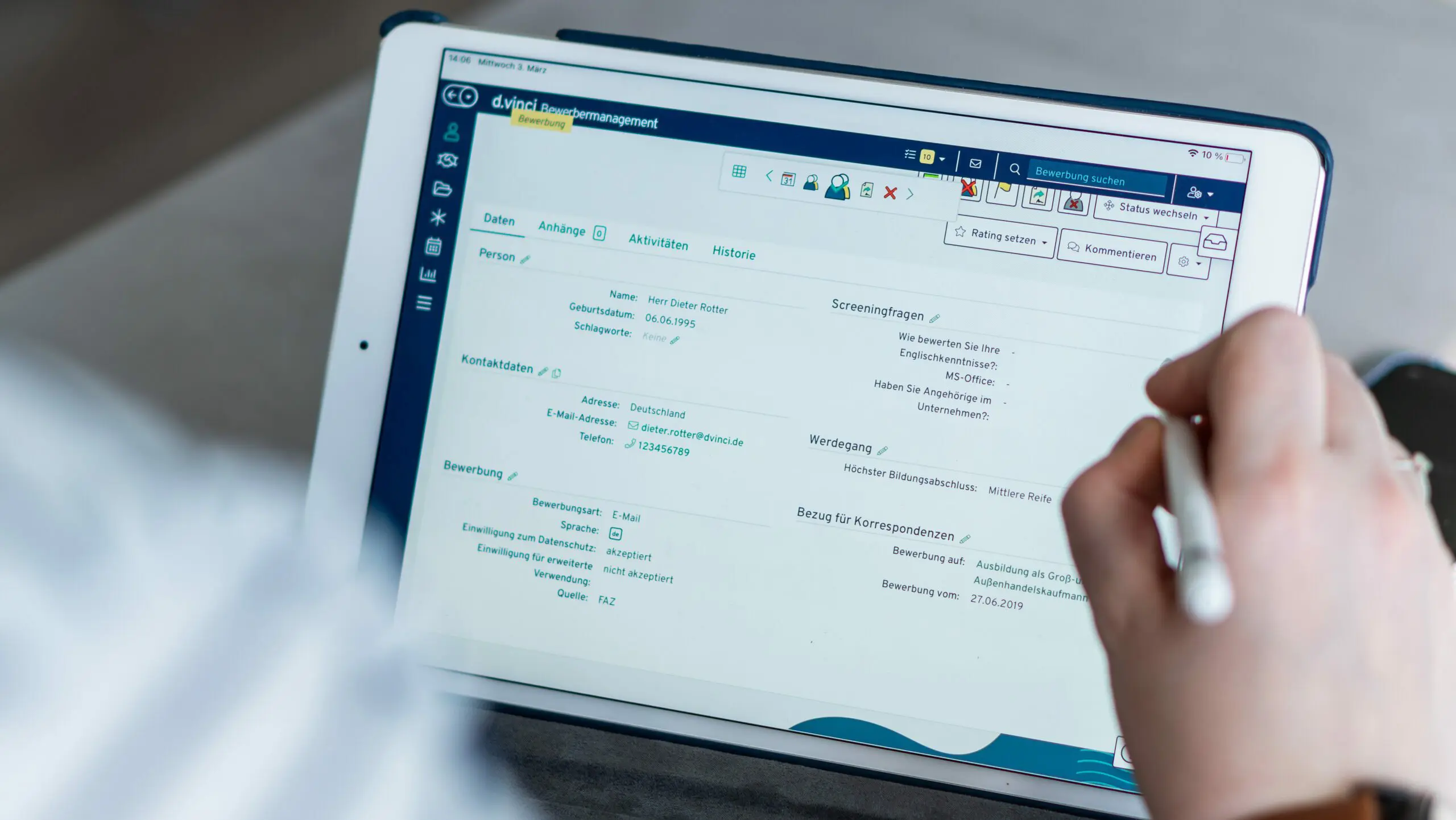 Ein Foto zeigt ein Tablet, auf welchem das d.vinci Bewerbermanagement geöffnet ist. Eine Hand tippt mit einem Touchpen darauf.