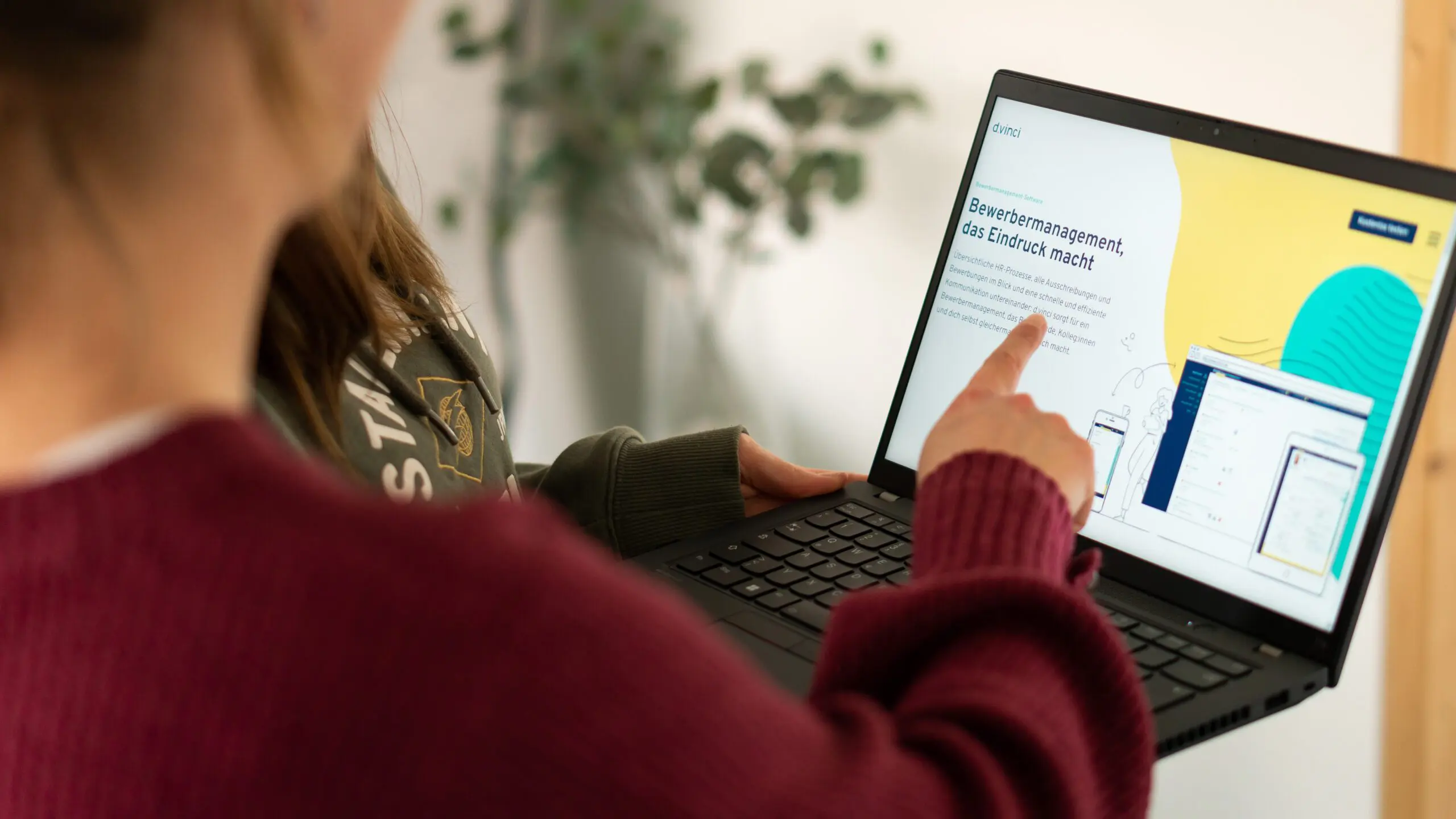 Ein Foto zeigt zwei Personen, die auf einen Laptop-Bildschirm zeigen. Auf dem Bildschirm ist die d.vinci-Bewerbermanagement-Seite geöffnet.